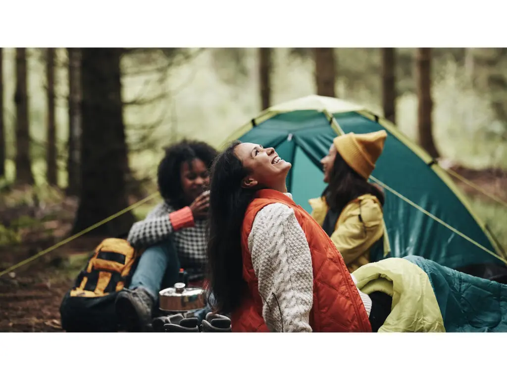 Image of friends camping in the woods and smiling.