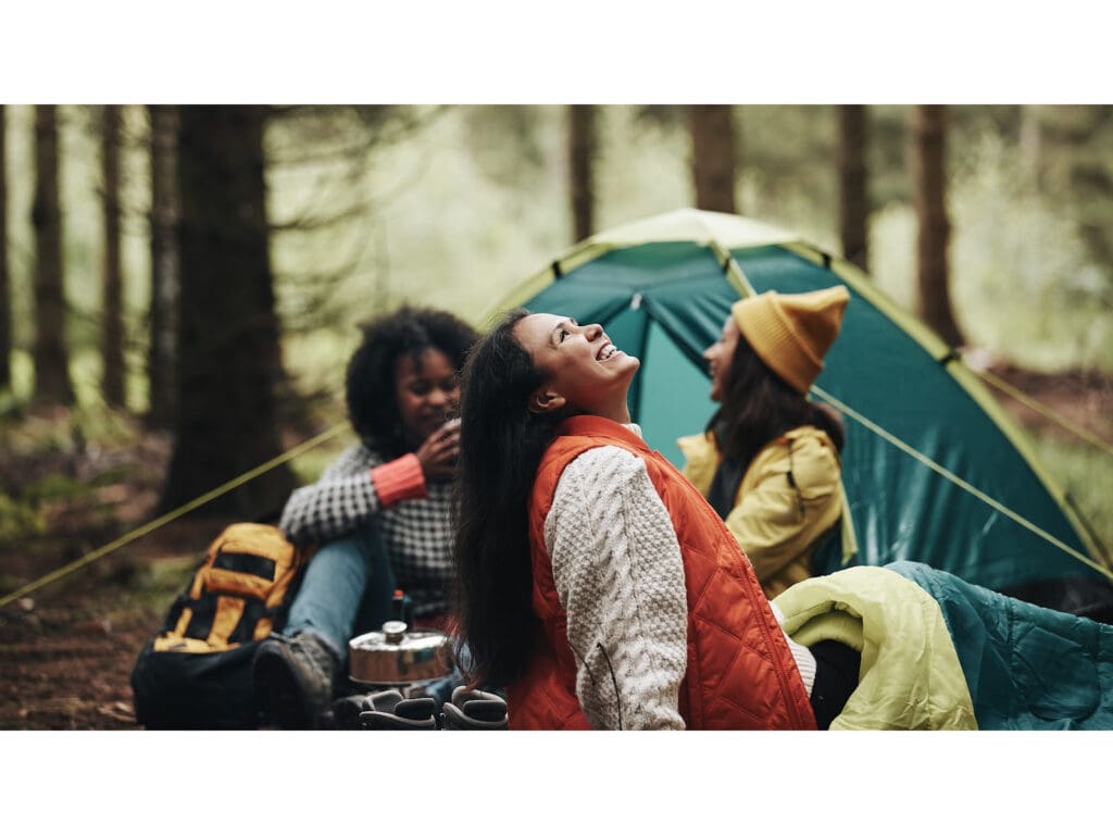 Image of friends camping in the woods and smiling.