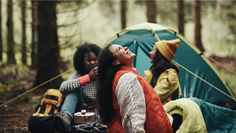 Image of friends camping in the woods and smiling.